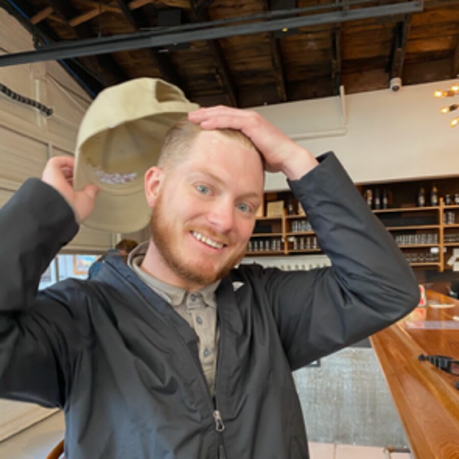 Alex Jay tipping a cap and grinning in a bar
