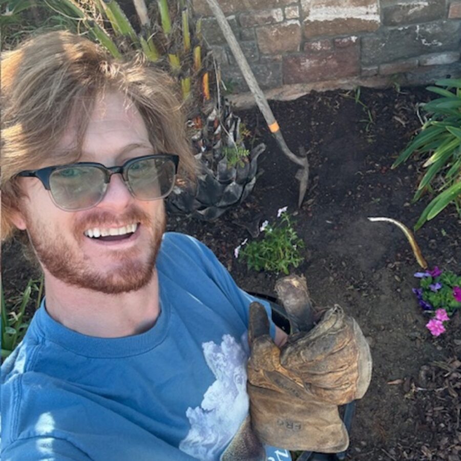 Alex Jay holding a work glove, smiling, in a garden bed